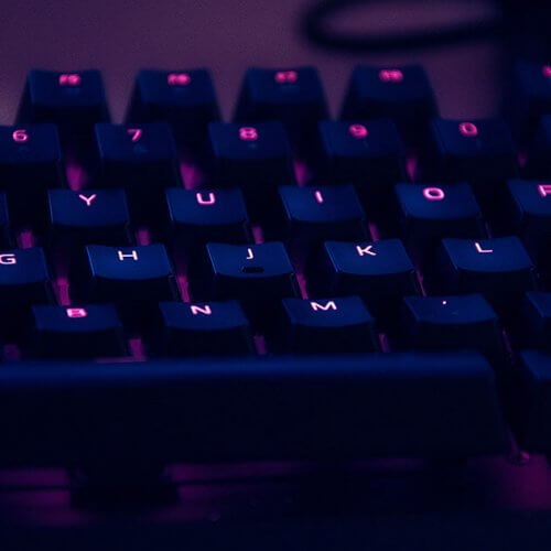 Un clavier d’ordinateur noir rétroéclairé en violet. De quoi rédiger un premier article de blog.