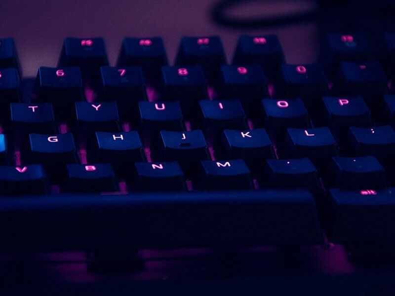 Un clavier d’ordinateur noir rétroéclairé en violet. De quoi rédiger un premier article de blog.